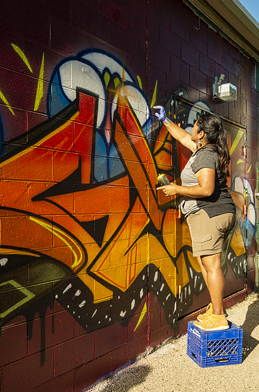 Woman on a milk crate painting a wall
